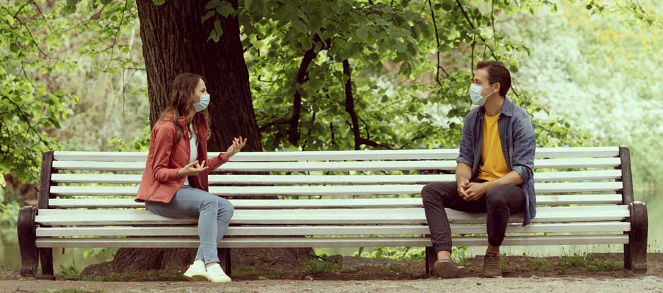kids-historical-fiction-books-written-about-covid-940x415px Teen couple in masks talking on park bench could feature in kids historical fiction about covid.