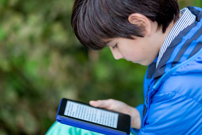 help for struggling readers as child uses kindle device to read more easily sitting outside in blue jacket